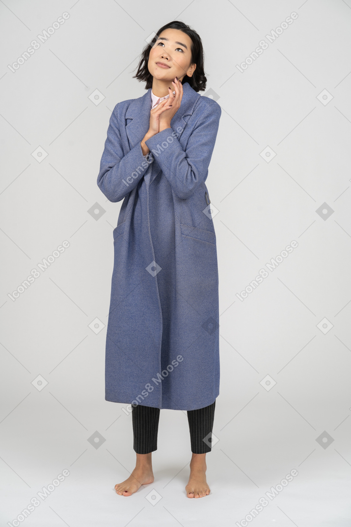 Woman in blue coat daydreaming with hands together