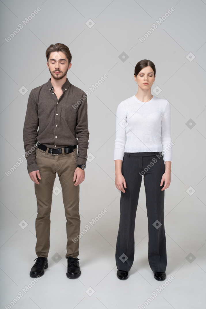 一对年轻夫妇在办公室服装站着，她的眼睛保持关闭的前视图