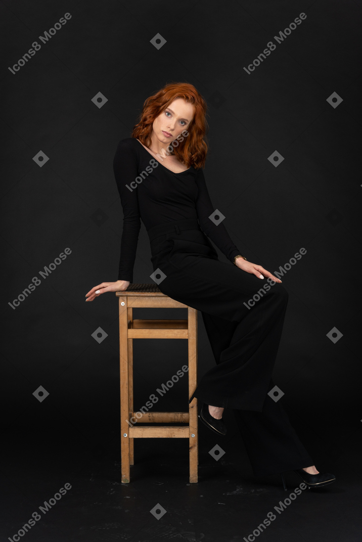 A side view of the cute young woman sitting on the high wooden chair