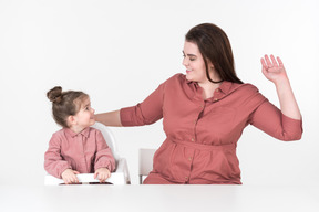 Mother and her little daughter, wearing red and pink clothes, having fun at the dinner table