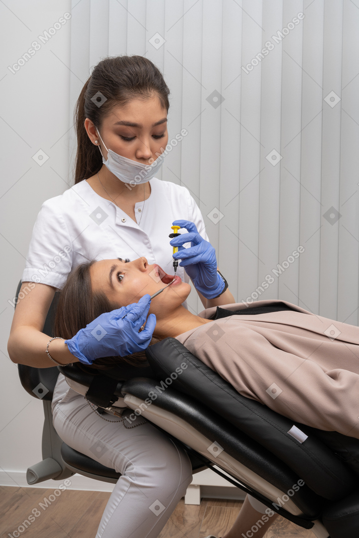 彼女の患者に注射をしているマスクとラテックス手袋の女性歯科医