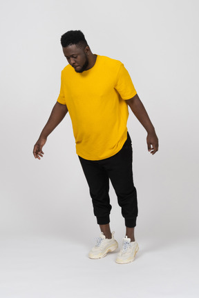 Vista de três quartos de um jovem de pele escura em uma camiseta amarela inclinado para a frente e esticando o braço