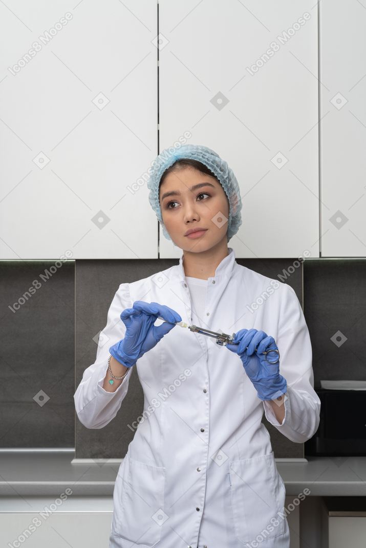 Front view of a female doctor in a medical hat holding a syringe and looking aside