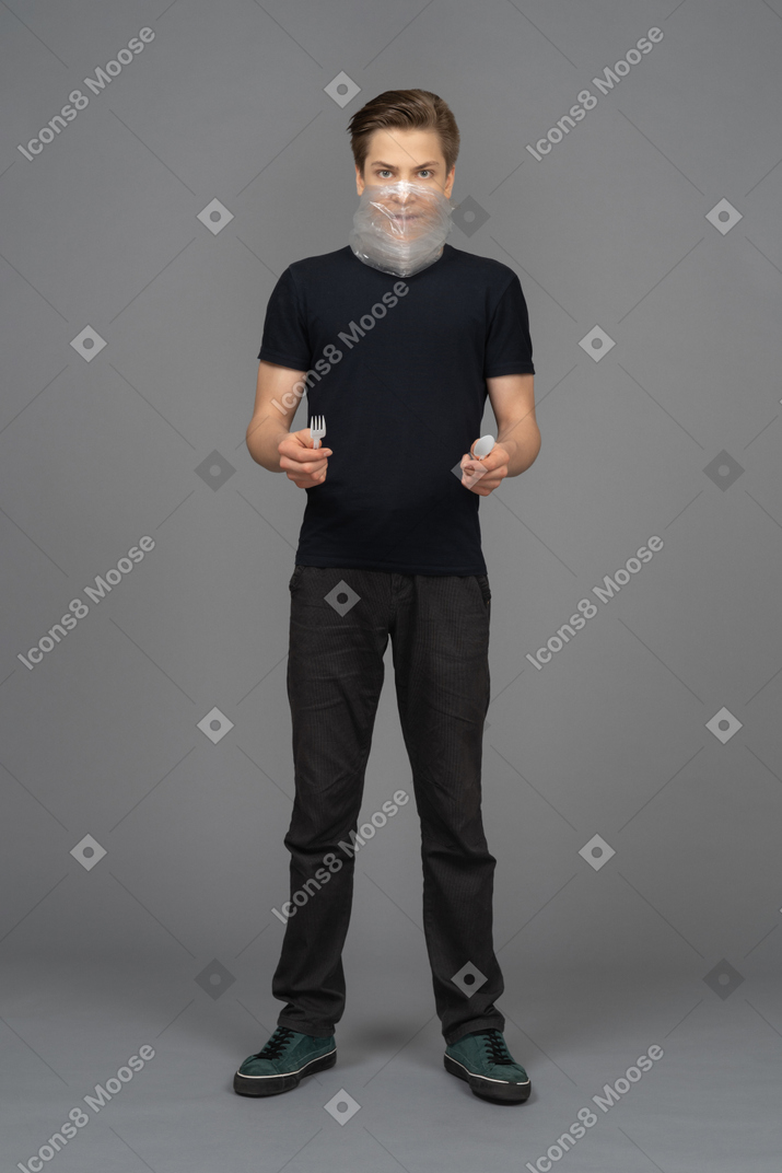 Man with plastic wrap over his mouth holds plastic spoon and knife