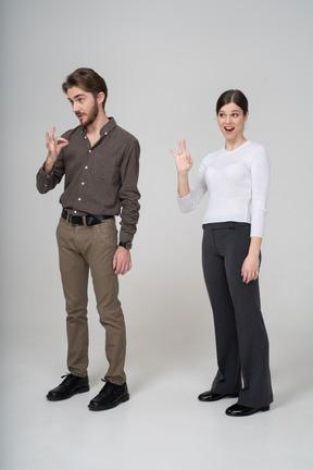 一对年轻夫妇在办公室服装显示ok的手势的四分之三视图