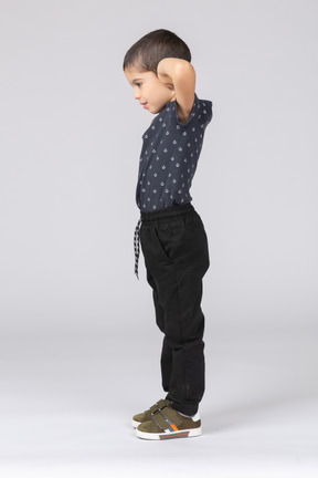 Vue latérale d'un garçon mignon posant avec les mains derrière la tête