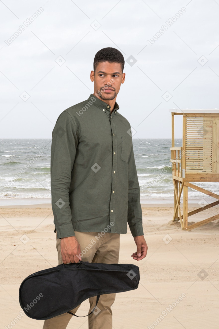 Hombre de pie en una playa con bolsa de ukelele
