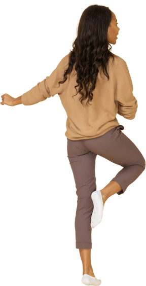 行進する浅黒い肌の若い女性の脚を上げるの4分の3の背面図