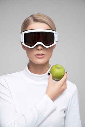 Mujer rubia con gafas de esquí sosteniendo manzana verde