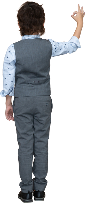 Vista trasera de un niño con traje gris que muestra el signo de ok