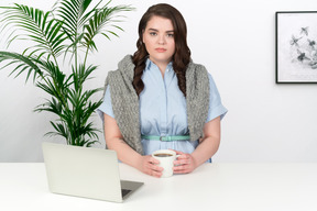 Woman sitting at office desk and holding cup of coffee