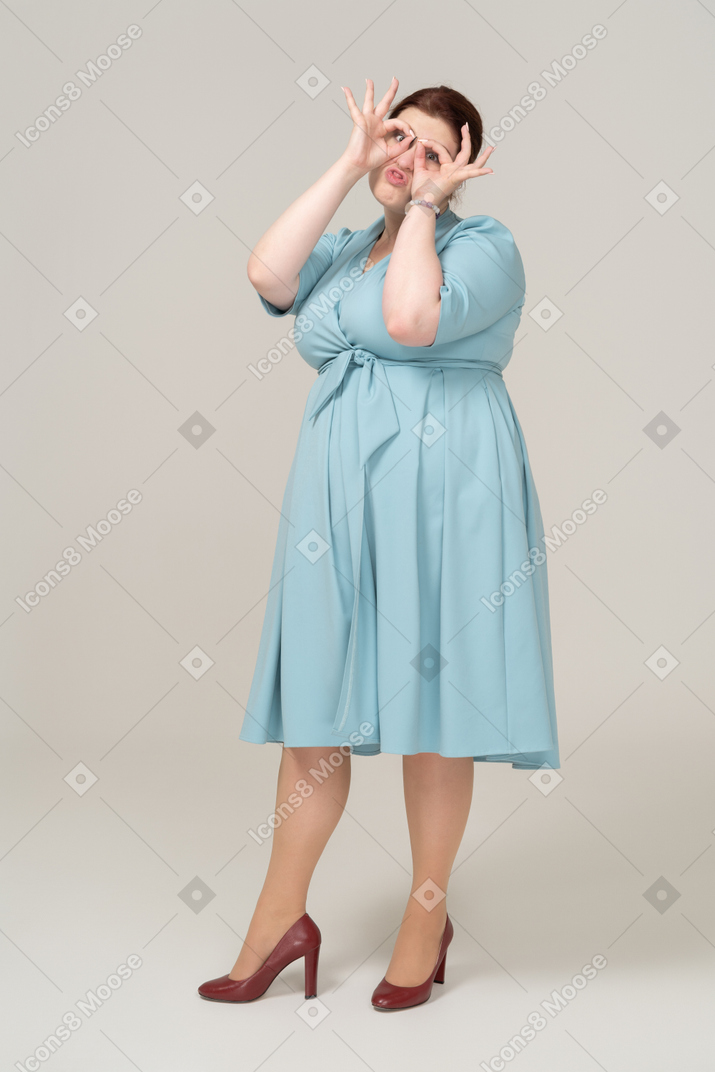 Front view of a woman in blue dress looking through imaginary binoculars