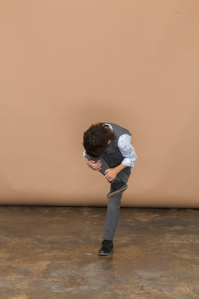 Vista frontal de un niño con traje gris que sufre de dolor en la pierna