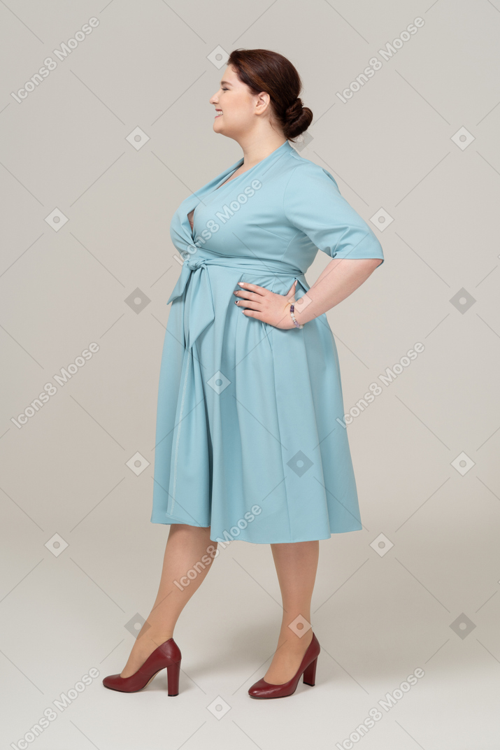 Vista laterale di una donna felice in abito blu in piedi con le mani sui fianchi