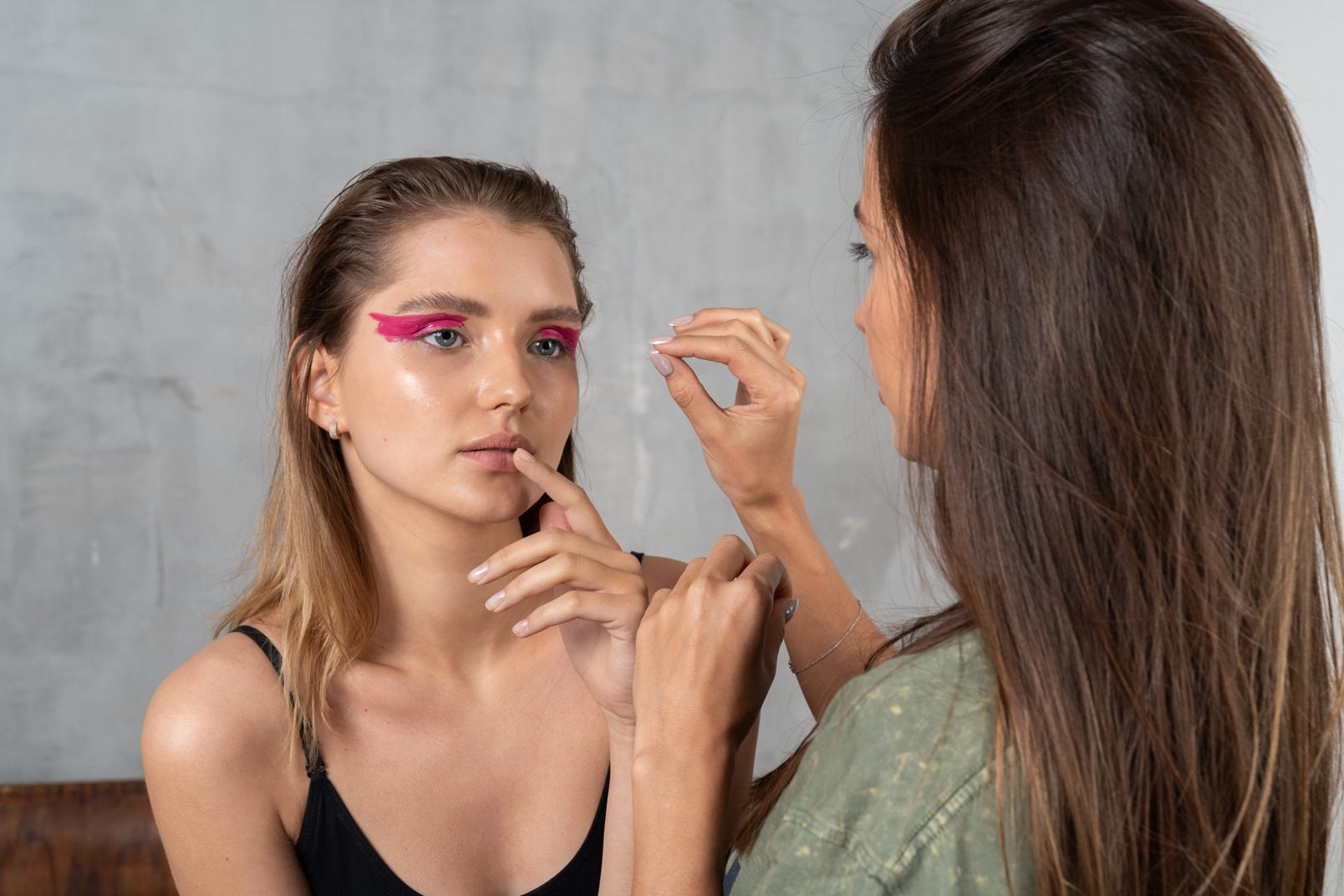 Front view of a young woman with bright pink eye make-up & her make-up artist