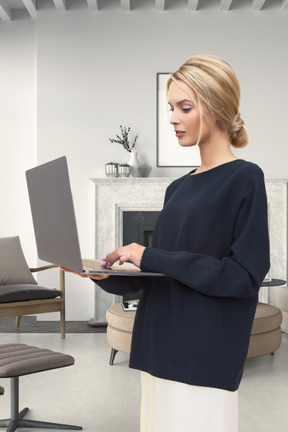 A woman standing in a living room using a laptop computer