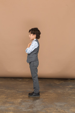 Vista lateral de um menino de terno cinza posando com braços cruzados