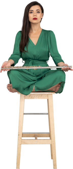 A figura intera di una giovane donna che tiene il suo clarinetto sulle ginocchia mentre è seduta su una sedia di legno