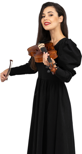 Крупный план улыбающейся молодой женщины в черном платье, играющей на скрипке