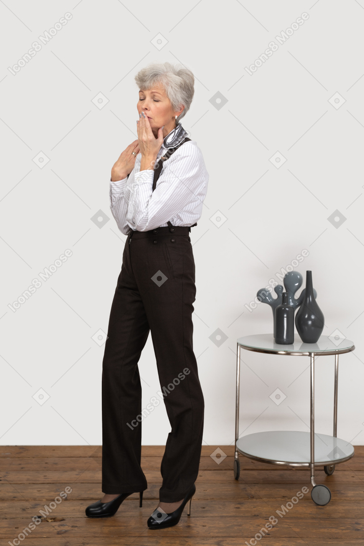Three-quarter view of a silent old lady in office clothing touching her mouth