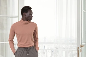 A man standing in front of a window with his hands in his pockets