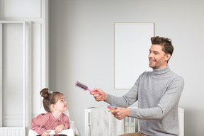 A happy father trying to teach his daughter to do her hair herself