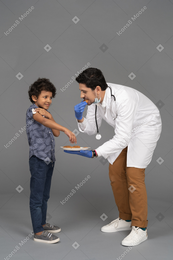 Niño y médico comiendo galletas después de la vacunación