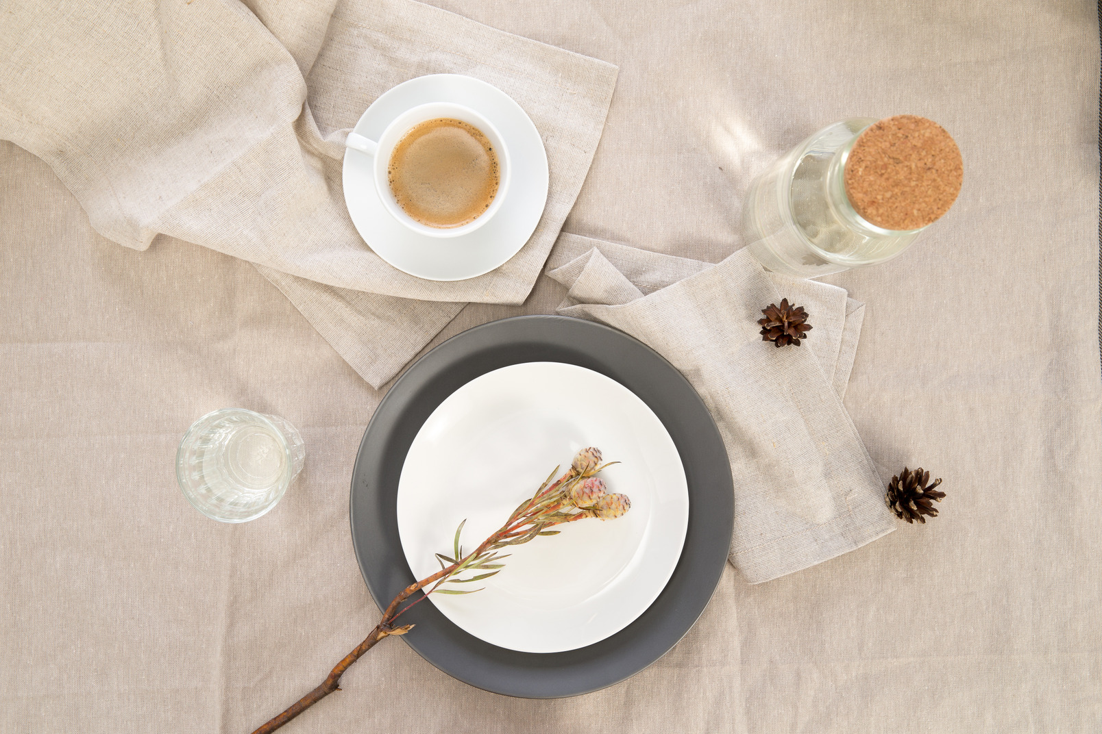 Black and white plates with flower twigs, moka, cup of coffee, glass bottle and glass of water on tablecloth