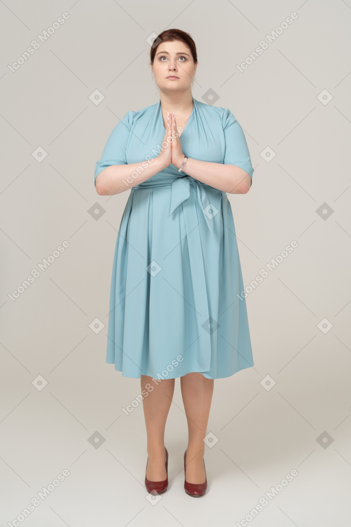 Vista frontal de una mujer en vestido azul haciendo gesto de oración