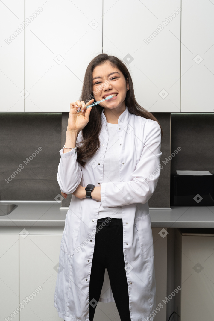 Front view of a female dentist brushing her teeth and looking at camera while narrowing eyes