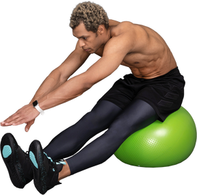 Three-quarter view of a shirtless afro man stretching while sitting on a green gym ball