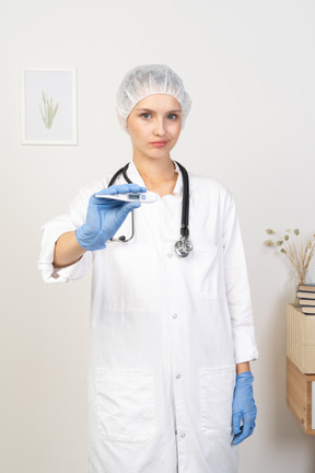 Vista frontale di una giovane dottoressa con lo stetoscopio che tiene il termometro