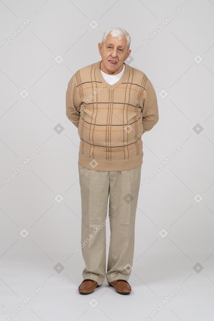 Front view of an old man in casual clothes standing with hands behind back and looking at camera