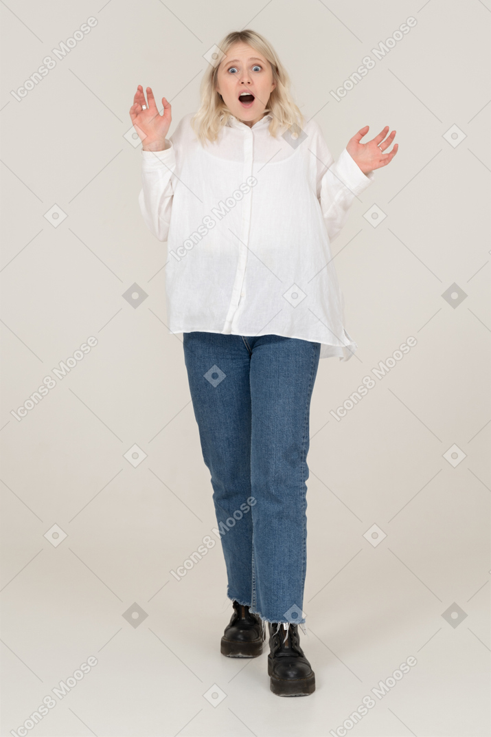 Vista frontal de una mujer rubia levantando las manos y mirando a la cámara con la boca abierta