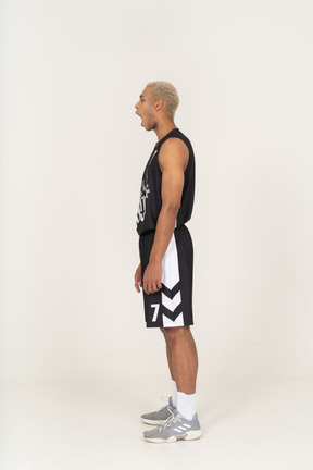 じっと立っているあくびをしている若い男性のバスケットボール選手の側面図