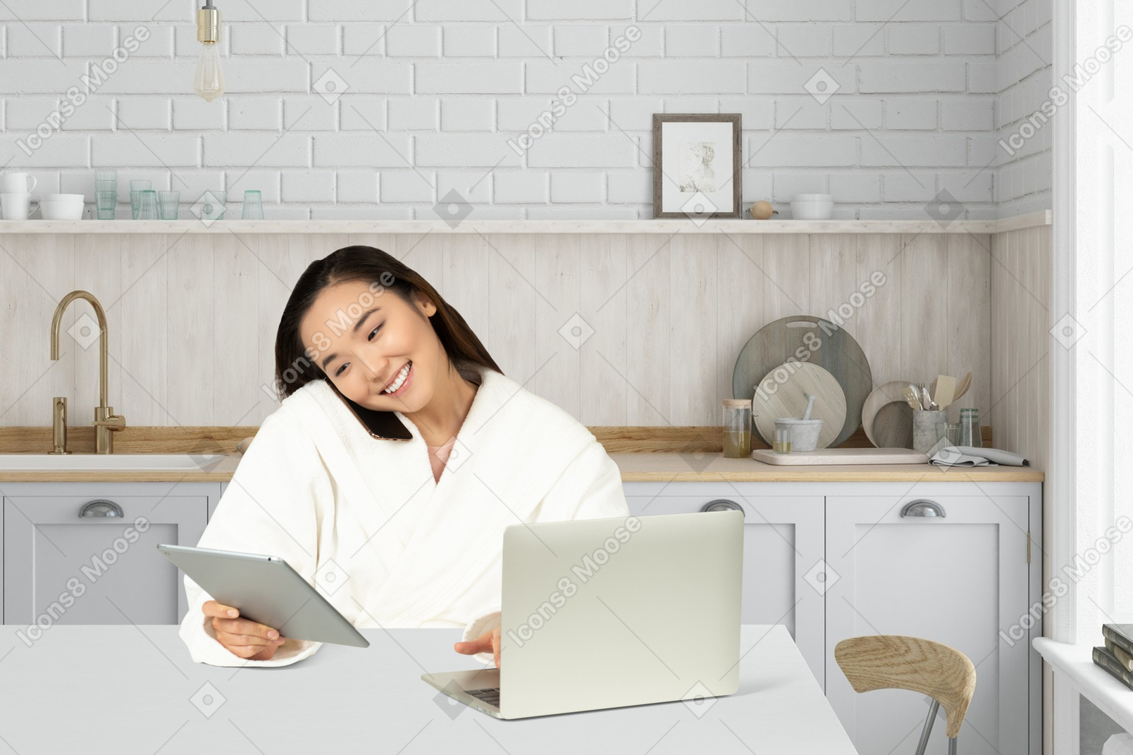 Woman in bathrobe sitting at a table using tablet and laptop