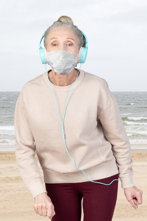 Elderly woman walking in face mask and listening to music
