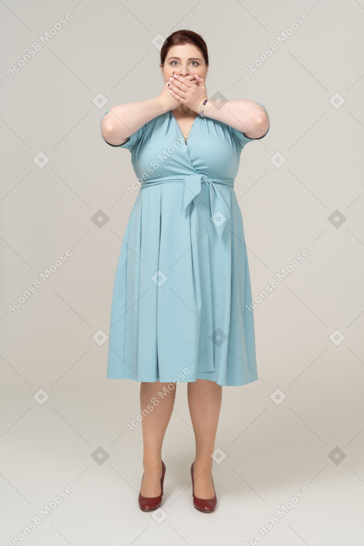 Front view of a woman in blue dress covering her mouth with hands