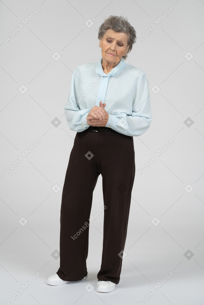 Front view of an old woman clasping hands sadly