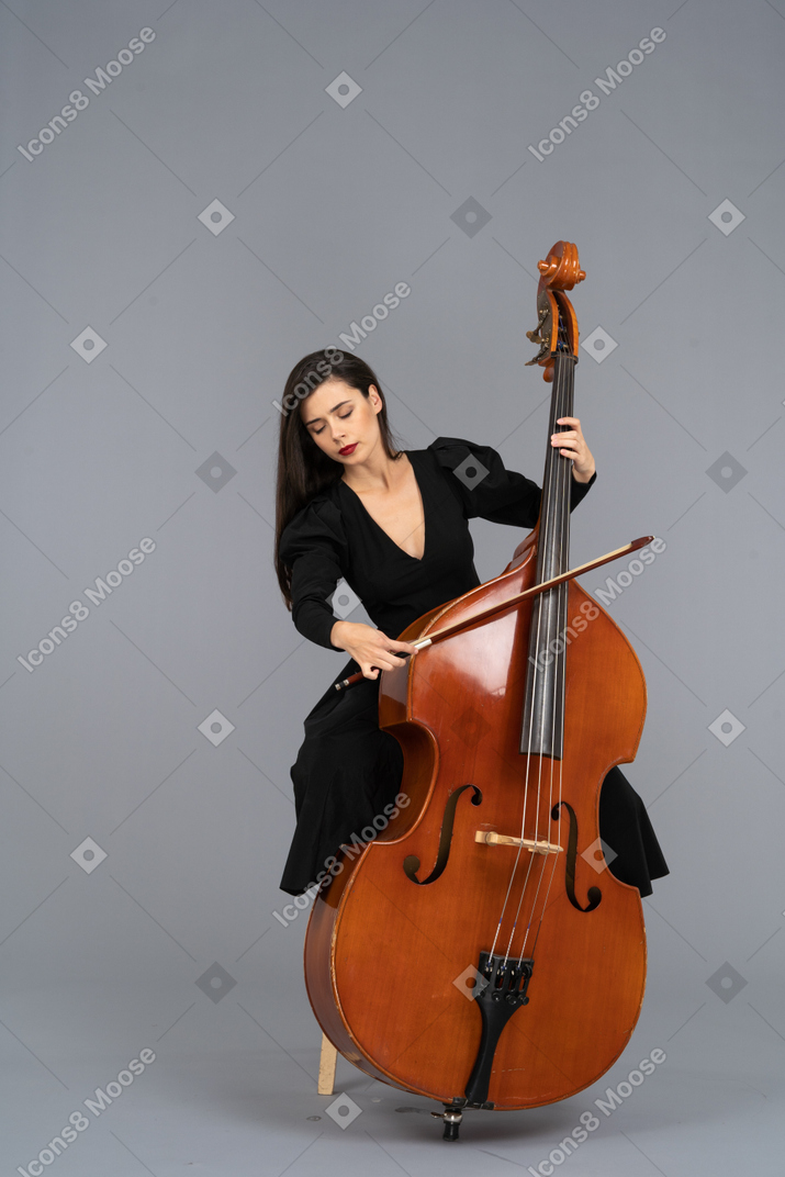 Front view of a young lady sitting on a chair while playing double-bass with a bow