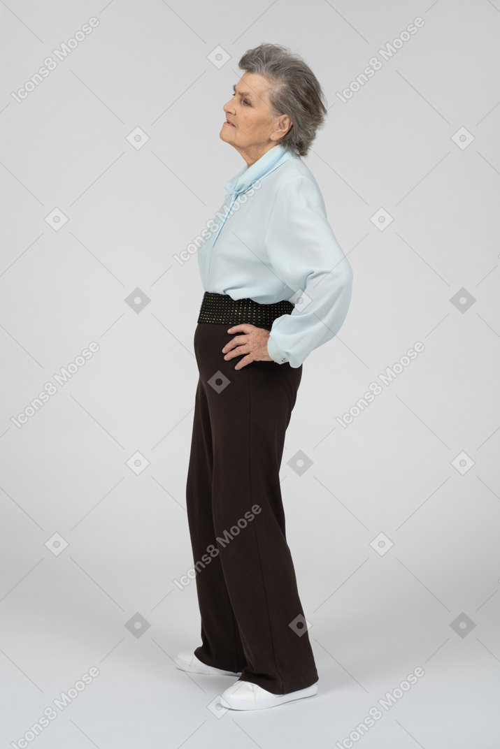 Vista lateral de una anciana que parece cansada con una mano en la cadera