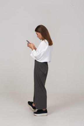 Dreiviertelansicht einer jungen dame in bürokleidung, die den feed per telefon überprüft