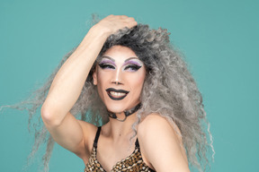 Headshot of a drag queen smiling with hand on top of head