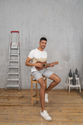 Three-quarter view of a man playing ukulele on a stool