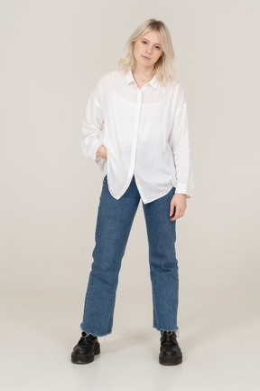 Front view of a blonde female in casual clothes putting hand in pocket and looking at camera