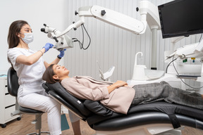 Pleine longueur d'une femme dentiste examinant sa patiente et regardant à travers le microscope