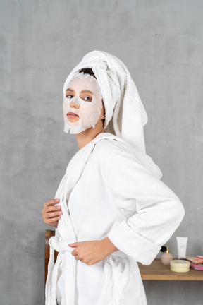 Vista lateral de uma mulher de roupão de banho com uma máscara facial