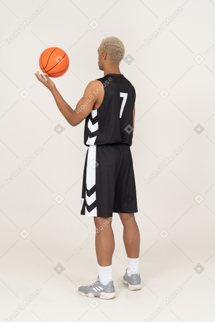 Vista posterior de tres cuartos de un joven jugador de baloncesto masculino sosteniendo una pelota