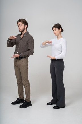 Vista di tre quarti di una giovane coppia in abiti da ufficio che mostra le dimensioni di qualcosa