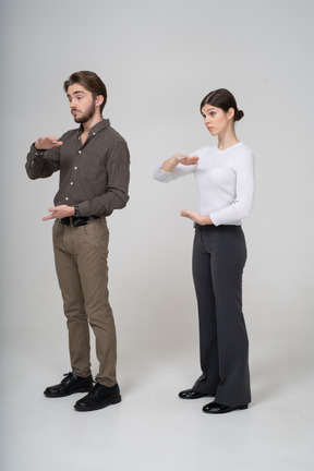 Vue de trois quarts d'un jeune couple en tenue de bureau montrant la taille de quelque chose